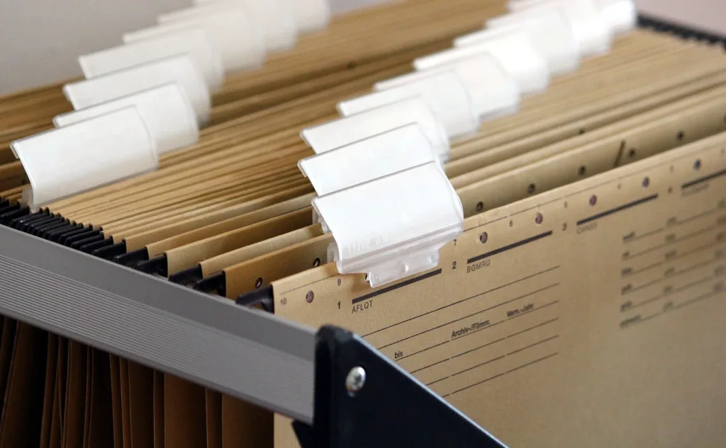A stack of printed documents beside a laptop showing a PDF